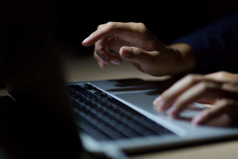 Close up of a man’s hands on keyboard of lap top in the dark room.