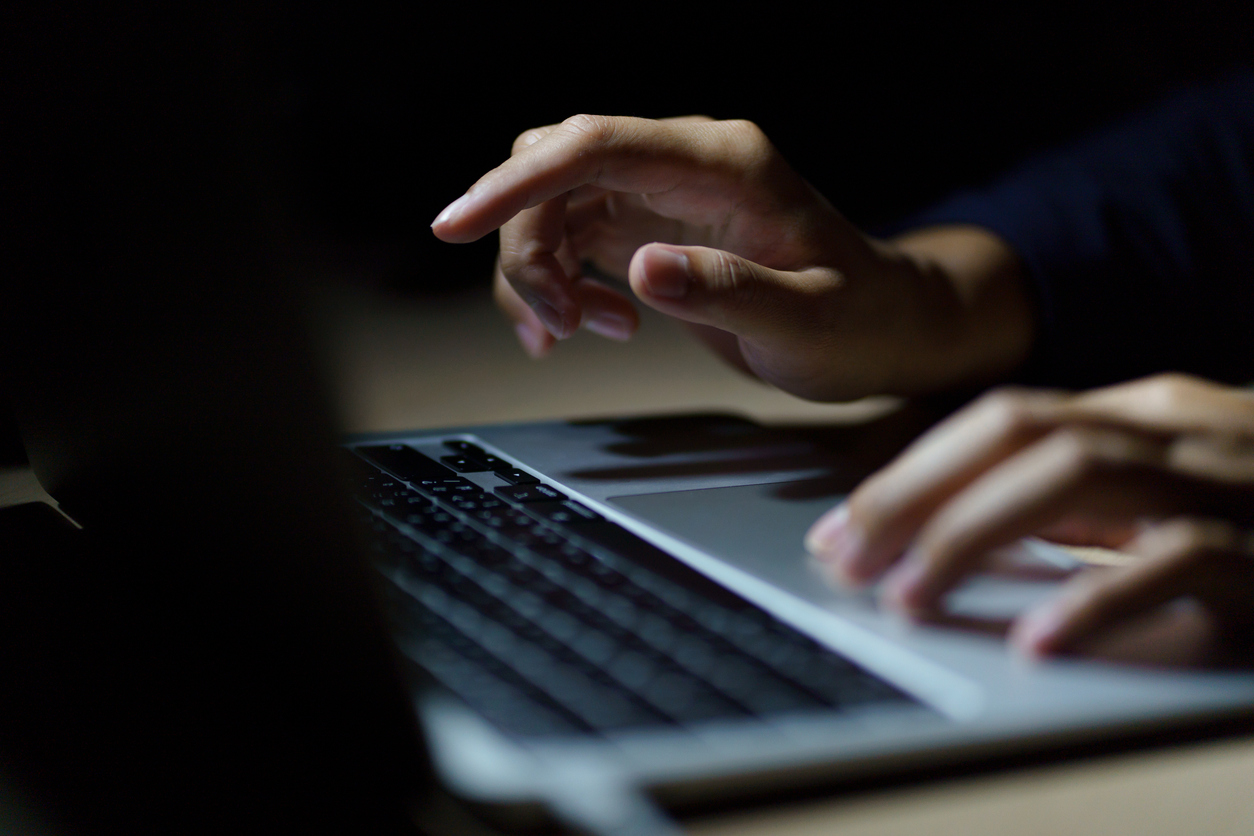Close up of a man’s hands on keyboard of lap top in the dark room.